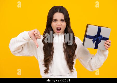 Angry face, upset emotions of teenager girl. Child teen girl with gift on yellow isolated background. Birthday, holiday present concept. Stock Photo