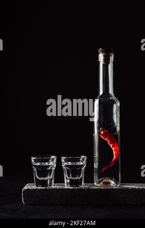 Two shot glasses and a bottle of vodka with red hot peppers. Stock Photo