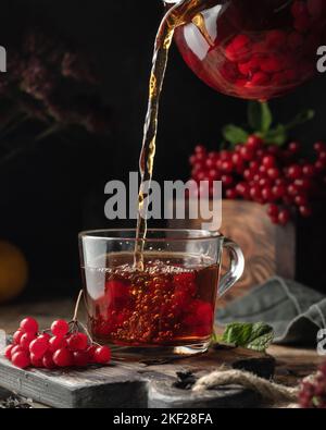 Viburnum tea is poured into a cup from a glass teapot with steam ...