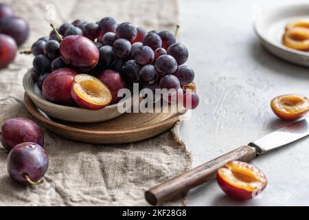 Ripe grapes and plums on linen tablecloth with knife, selective focus. Autumn mood still life composition. Horisontal orientation Stock Photo