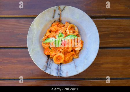 A plate of just cooked homemade fettuccine pasta with creamy tomato sauce, seafood and parmesan cheese, decorated with basil leaves on the wooden back Stock Photo