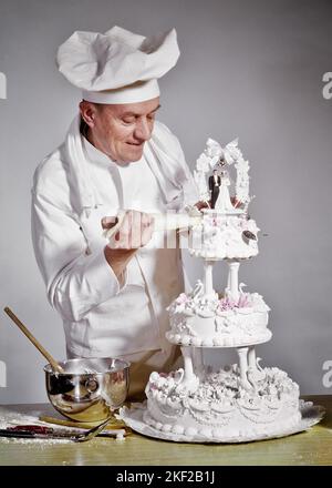 1960s PASTRY CHEF IN WHITE LINEN UNIFORM HAT TOQUE ADDING A TOUCH UP OF ICING TO TOP LAYER OF ELABORATE THREE TIER WEDDING CAKE - kf3687 HAR001 HARS SWEET JOY LIFESTYLE CELEBRATION MARRIED JOBS STUDIO SHOT BAKER CAKES EVENT SPOUSE HUSBANDS COPY SPACE HALF-LENGTH MARRIAGE PERSONS INSPIRATION MALES PROFESSION SUGAR CONFIDENCE CEREMONY ICING MIDDLE-AGED UTENSILS MIDDLE-AGED MAN PASTRY LINEN SKILL OCCUPATION SKILLS BAKE CUSTOMER SERVICE ADDING CUSTOM CAREERS LAYER TRADITION OCCASION FROSTING PRIDE UP OCCUPATIONS TIER MIXING BOWLS CREATIVITY TOQUE WIVES BRIDE AND GROOM CAUCASIAN ETHNICITY ELABORATE Stock Photo