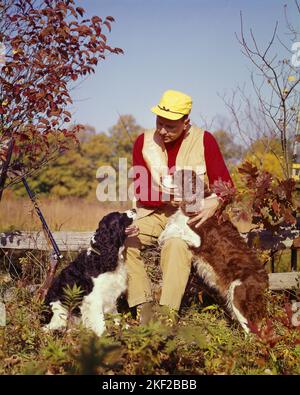 1960s MAN HUNTER WEARING YELLOW HAT RED SHIRT TAN VEST SITTING ON FENCE WITH TWO SPRINGER SPANIEL BIRD GUN DOGS  - kg2793 HAR001 HARS SEATED COPY SPACE FRIENDSHIP HALF-LENGTH PERSONS MALES HUNTER VEST HUNT RESTING HAPPINESS MAMMALS HIGH ANGLE ADVENTURE CANINES RECREATION FALL SEASON SPRINGER PETTING POOCH CONNECTION CONCEPTUAL SPRINGER SPANIEL CANINE COOPERATION FIREARM FIREARMS HUNTERS MAMMAL MID-ADULT MID-ADULT MAN TAN AUTUMNAL BIRD DOG CAUCASIAN ETHNICITY FALL FOLIAGE HAR001 OLD FASHIONED Stock Photo