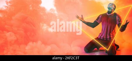 African american male player kneeling with illuminated triangle over peach smoky background Stock Photo