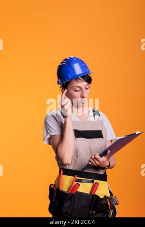 Woman contractor brainstorming ideas with clipboard files in studio, taking notes on papers and thinking about renovating solution. Industrial engineer using measurements to build site. Stock Photo