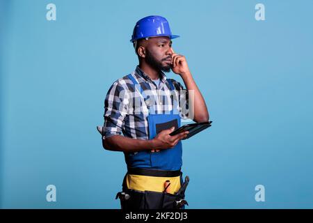 Portrait of african american contractor with digital tablet calculating costs and quantity of materials needed to perform the renovation. Supervisor using estimating application on electronic device. Stock Photo