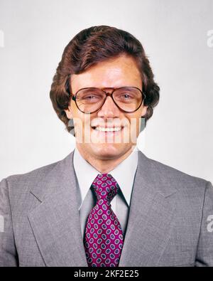 1970s MAN SMILING PORTRAIT WEARING GRAY BUSINESS SUIT PURPLE TIE AVIATOR EYEGLASSES FASHION  - kp2906 HAR001 HARS PROFESSION CONFIDENCE EYEGLASSES EYE CONTACT WHITE COLLAR SUIT AND TIE PURPLE HAPPINESS HEAD AND SHOULDERS CHEERFUL STYLES NECKTIE SMILES AVIATOR JOYFUL STYLISH AVIATOR FRAMES FASHIONS GRAY MID-ADULT MID-ADULT MAN PEOPLE ADULTS CAUCASIAN ETHNICITY HAR001 OLD FASHIONED Stock Photo