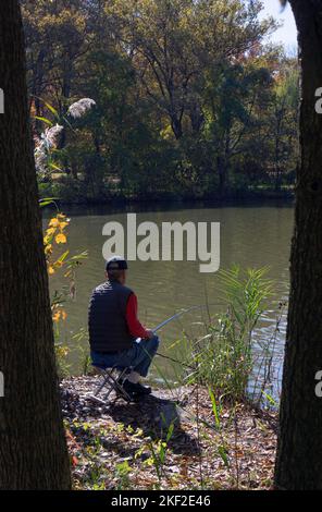 A retired man fishing in a quiet lake spot in Kissena Park in Flushing, New York. Stock Photo