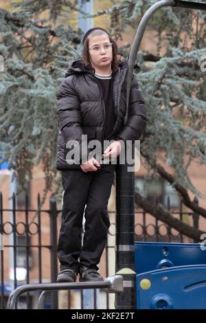 During recess at his yeshiva, an orthodox Jewish boy with peyot stands on equipment at Sobel Playground in Brooklyn, New York. Stock Photo