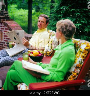 1970s COUPLE MAN AND WOMAN TALKING READING NEWSPAPER SITTING IN PATIO CHAIRS ON BACKYARD BRICK PATIO TERRACE  - ks15162 HAR001 HARS STYLE COMMUNICATION YOUNG ADULT INFORMATION LIFESTYLE BRICK FEMALES MARRIED PATIO SPOUSE HUSBANDS HOME LIFE COPY SPACE FRIENDSHIP HALF-LENGTH LADIES PERSONS MALES NEWSPAPERS PARTNER BEVERAGE LEISURE STYLES TO CONNECTION STYLISH FASHIONS MID-ADULT MID-ADULT MAN MID-ADULT WOMAN RELAXATION TERRACE TOGETHERNESS WIVES CAUCASIAN ETHNICITY HAR001 OLD FASHIONED Stock Photo