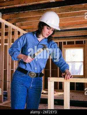 1970s DIY BRUNETTE WOMAN WORKING AS CARPENTER ON CONSTRUCTION SITE USING HAMMER AND NAILS WEARING DENIM WORK CLOTHES HARD HAT - ks15247 VRE001 HARS COTTON LIFESTYLE SATISFACTION NAIL FEMALES VERTICAL JOBS SITE CARPENTER COPY SPACE HALF-LENGTH PERSONS INSPIRATION NAILS CONFIDENCE DENIM WOMAN'S BRUNETTE BLUE COLLAR OCCUPATION PROTECT STRUCTURE WORKMEN BEAM MANUAL PROTECTION HARD HAT AND WOMAN'S LIBERATION WOMEN'S RIGHTS LIB LOW ANGLE WOMAN'S RIGHTS WORKFORCE WOMEN'S LIB WOMEN'S LIBERATION LABOR PRIDE RIGHTS LABORERS OPPORTUNITY HARDHAT OCCUPATIONS USING HAMMERS NAILING CONSTRUCTION SITE Stock Photo