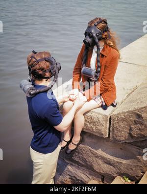 1960s 1970s YOUNG COUPLE STONE PIER HOLDING HANDS WOMAN SITTING WEARING GAS MASKS  - ks6901 HAR001 HARS FEMALES MASKS NATURE COPY SPACE FRIENDSHIP HALF-LENGTH LADIES PERSONS INSPIRATION CARING DANGER MALES RISK TEENAGE BOY HAZARD SADNESS PIER DISASTER DREAMS HIGH ANGLE DANGEROUS ENVIRONMENT PROTECTION POISONOUS RISKY TO HAZARDOUS RELATIONSHIPS PERIL UNSAFE CLIMATE CHANGE CONNECTION CONCEPTUAL HARMFUL CONTAMINATION JEOPARDY TOXINS COOPERATION ENVIRONMENTAL GREENHOUSE GASES IDEAS SOLUTIONS TOGETHERNESS CAUCASIAN ETHNICITY HAR001 OLD FASHIONED Stock Photo