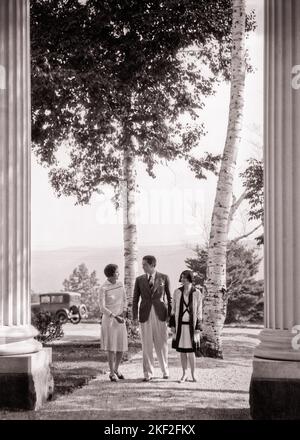 1920s 1930s ONE MAN WITH TWO WOMEN WALKING THROUGH COLUMNS ENTRANCE FASHIONABLY DRESSED UPSCALE  - o4550 HAR001 HARS COMMUNICATION CANADA FRIEND YOUNG ADULT WEALTHY VACATION MYSTERY RICH LIFESTYLE HISTORY FEMALES RURAL HOME LIFE LUXURY COPY SPACE FRIENDSHIP FULL-LENGTH LADIES PERSONS MALES CONFIDENCE B&W SUCCESS TIME OFF SUIT AND TIE HAPPINESS LEISURE STYLES TRIP GETAWAY WEALTH COLUMNS HOLIDAYS UPSCALE CONCEPTUAL FASHIONABLY AFFLUENT FRIENDLY STYLISH FASHIONS MID-ADULT MID-ADULT MAN MID-ADULT WOMAN MUSKOKA TOGETHERNESS VACATIONS WELL-TO-DO YOUNG ADULT MAN YOUNG ADULT WOMAN BLACK AND WHITE Stock Photo