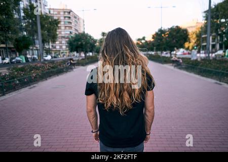 caucasian young man black t-shirt blond long hair from back standing on the boulevard in the city Stock Photo