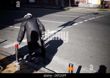 An old woman crosses the road during the day Stock Photo