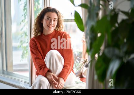 Pretty serene young woman sitting on windowsill relaxing at home. Portrait Stock Photo
