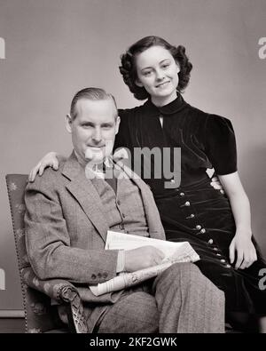 1930s 1940s PORTRAIT TEENAGE GIRL SITTING WITH HER ARM AROUND HER FATHER HOLDING A NEWSPAPER BOTH SMILING LOOKING AT CAMERA - s7385 HAR001 HARS NOSTALGIC AROUND PAIR BEAUTY HER OLD TIME NOSTALGIA OLD FASHION 1 JUVENILE STYLE STRONG PLEASED FAMILIES JOY LIFESTYLE FEMALES STUDIO SHOT HEALTHINESS HOME LIFE COPY SPACE FRIENDSHIP HALF-LENGTH DAUGHTERS PERSONS CARING MALES TEENAGE GIRL VEST FATHERS B&W EYE CONTACT HAPPINESS CHEERFUL DADS PRIDE SMILES CONNECTION THREE PIECE SUIT FATHER AND DAUGHTER JOYFUL STYLISH TEENAGED FATHERS AND DAUGHTERS PERSONAL ATTACHMENT AFFECTION COOPERATION EMOTION GROWTH Stock Photo