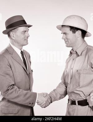 1950s 1960s SMILING BUSINESS MAN SHAKING HANDS WITH SMILING BLUE COLLAR WORKER WEARING HARD HAT - s8549 HAR001 HARS LIFESTYLE SATISFACTION JOBS STUDIO SHOT MANAGER COPY SPACE FRIENDSHIP HALF-LENGTH PERSONS MALES PROFESSION CONFIDENCE EXECUTIVES B&W SUCCESS SKILL SUIT AND TIE OCCUPATION SKILLS CAREERS LABOR OPPORTUNITY TO EMPLOYMENT OCCUPATIONS SHAKING HANDS BOSSES CONNECTION INFRASTRUCTURE EMPLOYEE COOPERATION MANAGERS MID-ADULT MID-ADULT MAN YOUNG ADULT MAN BLACK AND WHITE CAUCASIAN ETHNICITY HAR001 LABORING OLD FASHIONED Stock Photo