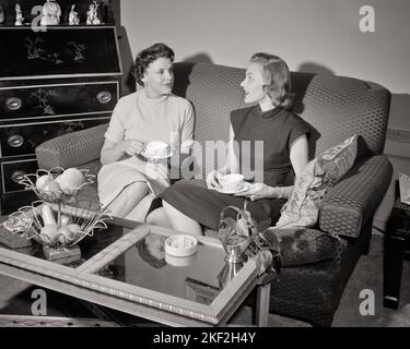 1950s TWO WOMEN SITTING ON SOFA HAVING CUP OF COFFEE VISITING TALKING GOSSIPING - s8943 DEB001 HARS INFORMATION LIFESTYLE FEMALES HOME LIFE COPY SPACE FRIENDSHIP HALF-LENGTH LADIES PERSONS CHAT GOSSIPING B&W BUZZ HIGH ANGLE BEVERAGE DISCOVERY FLUID BUSYBODY TELLING TO STORIES CONNECTION CONSUME CONSUMING FRIENDLY HYDRATION STYLISH VISITING DEB001 TATTLER CAFFEINE HEARSAY JOE COOPERATION JAVA MID-ADULT MID-ADULT WOMAN REFRESHING RUMORS TOGETHERNESS YOUNG ADULT WOMAN BEVERAGES BLACK AND WHITE CAUCASIAN ETHNICITY OLD FASHIONED Stock Photo