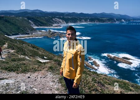 latin guy with yellow jacket standing looking at camera calm and relaxed near the sea from the nice cliffs, asturias, spain Stock Photo