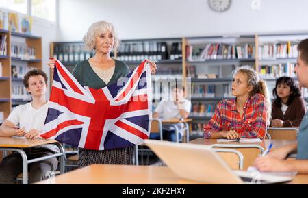 Elderly teacher shows the flag of Great Britain to teenagers and talks about this country during lesson at library school Stock Photo