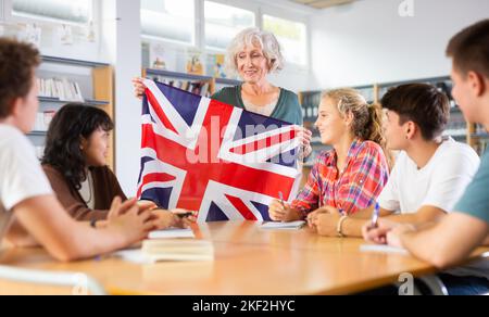 Elderly teacher shows the flag of Great Britain to teenagers and talks about this country during lesson at library school Stock Photo