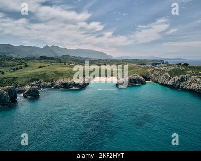small beach hidden between the grass, the vegetation and the large rocks that surround the coast in drone view from the sea, ribadesella asturias Stock Photo