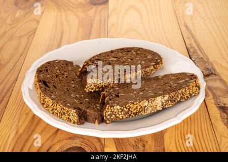 Three pieces of rye multigrain bread with a ceramic white plate on a wooden table, macro. Stock Photo