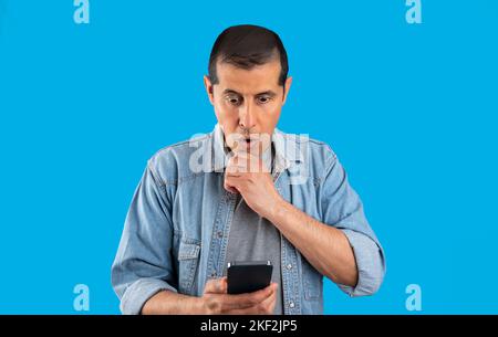 Handsome man using smartphone standing over isolated blue background serious face thinking about question very confused idea images Stock Photo