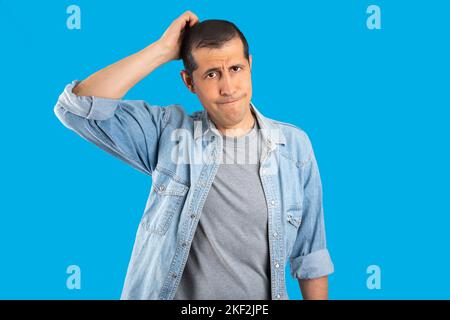 Handsome man over isolated blue background confuse and wonder about question. Uncertain with doubt, thinking with hand on head. Pensive concept Stock Photo