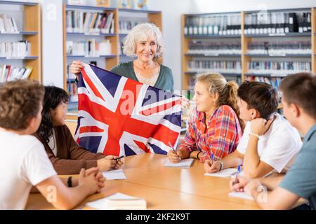 Elderly teacher shows the flag of Great Britain to teenagers and talks about this country during lesson at library school Stock Photo