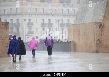 Valletta, Malta - November 12, 2022: People wearing rain ponchos and umbrellas walking on a rainy day Stock Photo