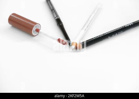 Lip gloss brush, brown lip pencil, black eye pencil and white eyeliner pencil on a white background; lips and eye makeup and cosmetics. Stock Photo