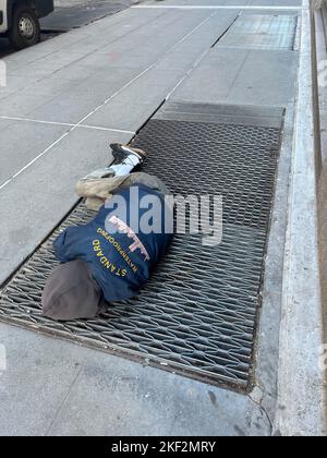 Man sleeps on a subway grate on a sidewalk where warm air rises in Manhattan, New York City. Stock Photo