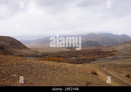 Autumn valley in the mountains with a winding river and an asphalt road running along its edge. Chuisky tract, Altai, Siberia, Russia. Stock Photo