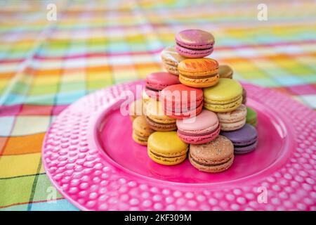 French pastry macarons tower presentation on pink dessert plate at bakery. Retro vintage checkered tablecloth table decor home kitchen. Assortment of Stock Photo