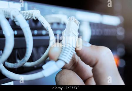 Hand on network cable in server room or data center for maintenance on server machine. Technology, connection and wires in datacenter, information Stock Photo