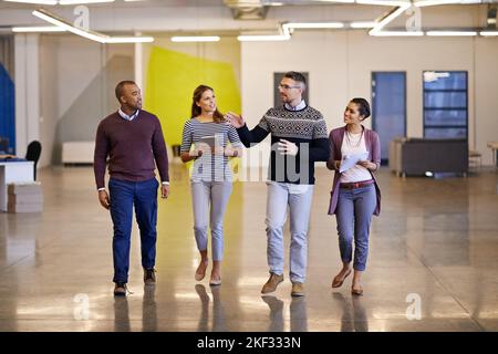 Together we can achieve greatness. a group of work colleagues walking next to each other in a straight line at work discussing plans. Stock Photo