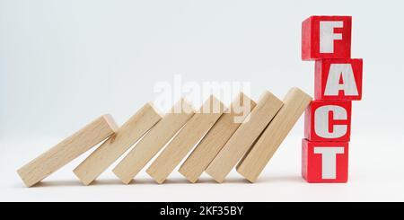 Business and economy concept. On a white background, wooden dice fell like dominoes, the fall was stopped by cubes with the inscription - FACT Stock Photo