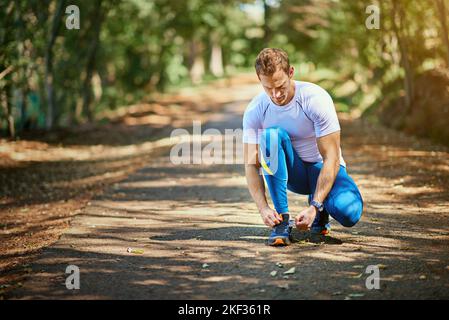 Lacing up. a young man tying his shoelaces before a trail run. Stock Photo