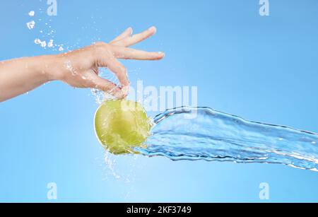 Hand, water and apple in studio on a blue background for health, diet or wellness. Food, splash and nutrition with a green fruit in the hands of a Stock Photo