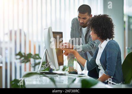 Trouble shooting is their specialty. designers talking together at a workstation in an office. Stock Photo