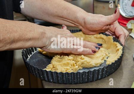 Cook kneads the dough in a mold for making a pie in the kitchen Stock Photo
