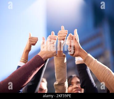 Heres to a great business. a group of people huddling together in a circle and showing thumbs up in the air. Stock Photo