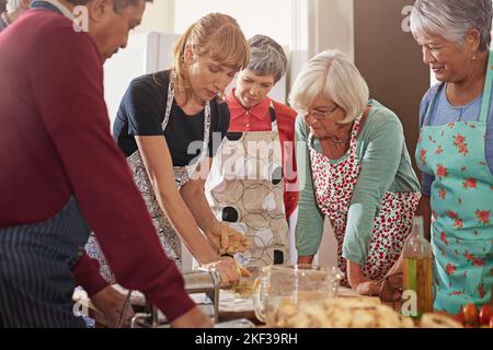 Showing them how to cut their kitchen time in half. a group of seniors attending a cooking class. Stock Photo