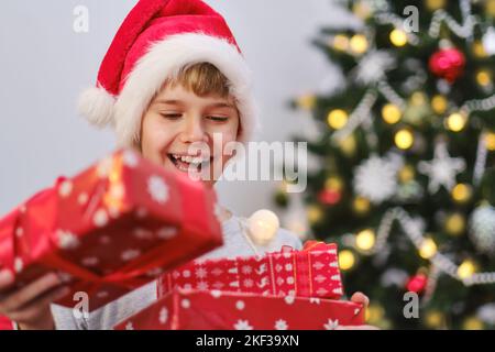 Portrait of an excited boy holding presents by the Christmas tree on Christmas morning. Stock Photo