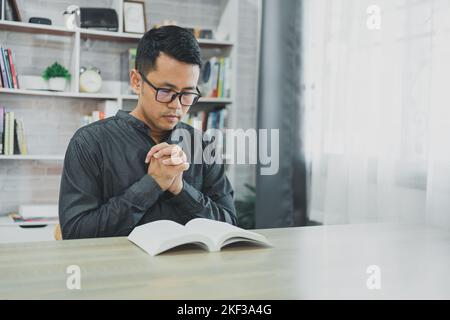 Asian man doing hands together in prayer to God along with the bible In the Christian concept of faith, spirituality and religion, men pray in the Bib Stock Photo
