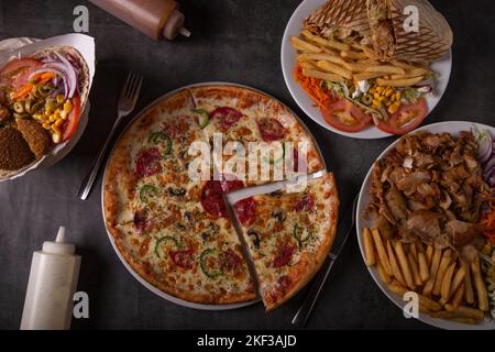 Top view of table scene with a variety of foods for take out or delivery. Beef and chicken kebab, pepperoni pizza and sauces, including fries. Stock Photo