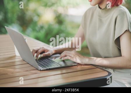 Crop image of asian freelance woman smile typing on keyboard and working on laptop on wooden table at home. Entrepreneur woman working for her busines Stock Photo