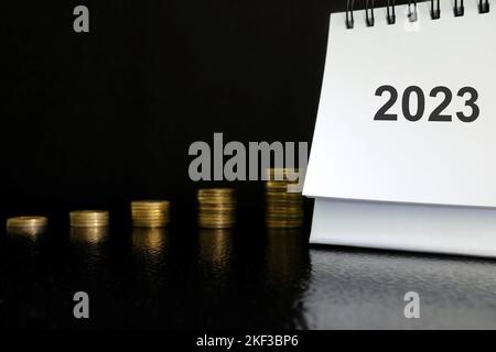 Year 2023 economy growth and recovery after crisis concept. 2023 desk calendar with increasing stack of coins on dark black background. Stock Photo